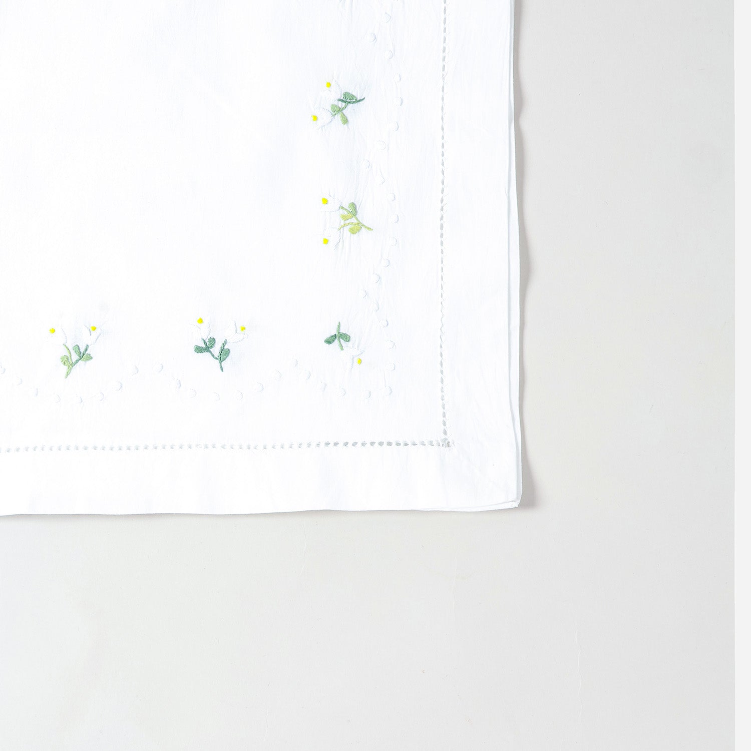 Detailed corner view of a handcrafted table runner featuring elegant daisy embroidery on a white cotton background