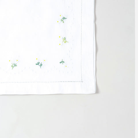Detailed corner view of a handcrafted table runner featuring elegant daisy embroidery on a white cotton background