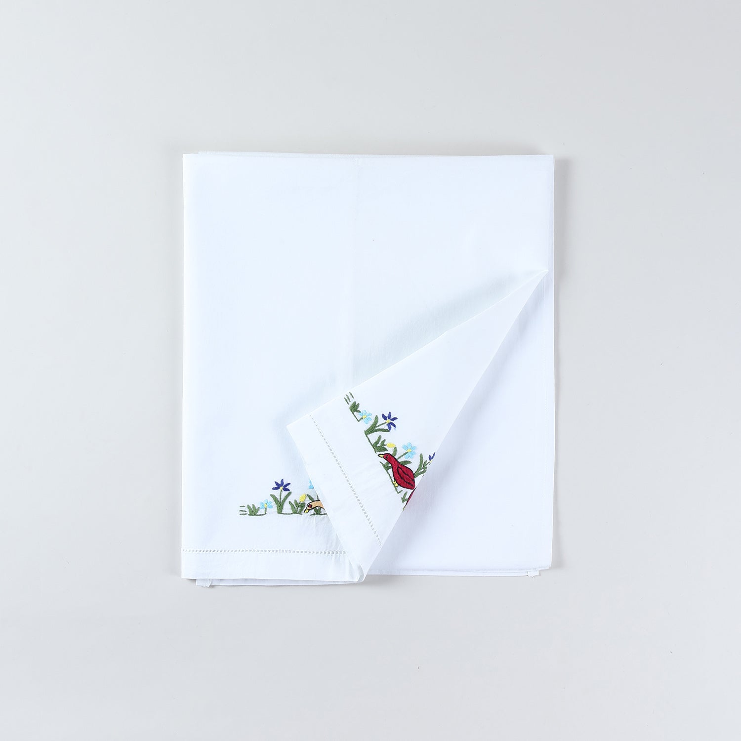 Cotton kids bedsheet folded back diagonally to showcase both colourful duck embroidery styles with Bengal Chikankari hand embroidery on white fabric