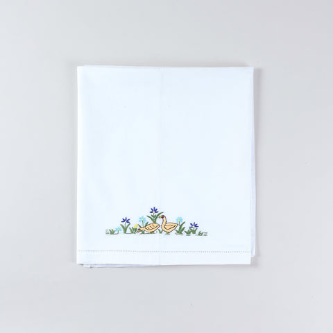 White cotton kids' bedsheet folded diagonally to display two distinct multi-coloured duck motifs created with hand embroidery on a soft cotton base