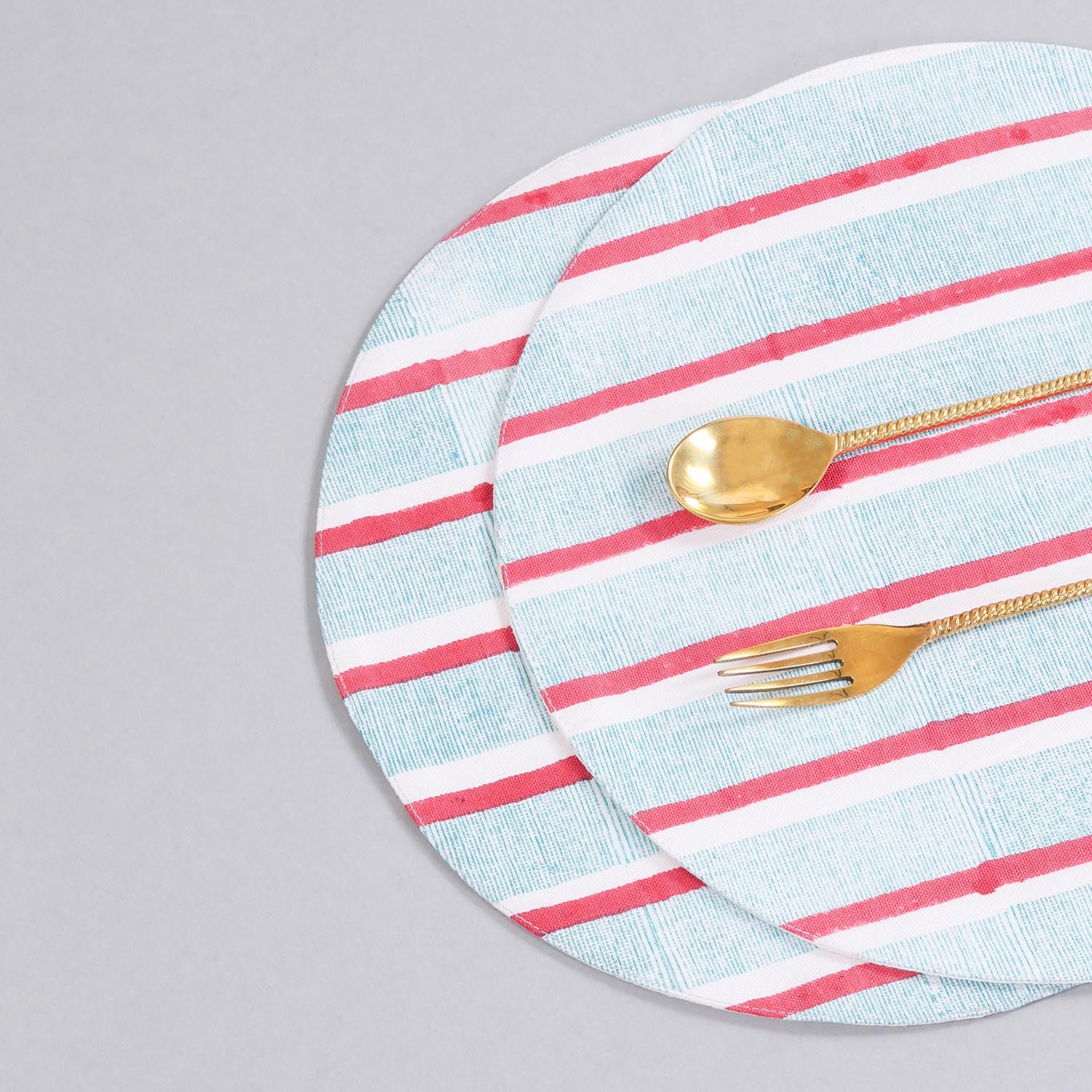 Styled view of a round cotton placemat showcasing red and green stripe block-printed detailing and handcrafted craftsmanship
