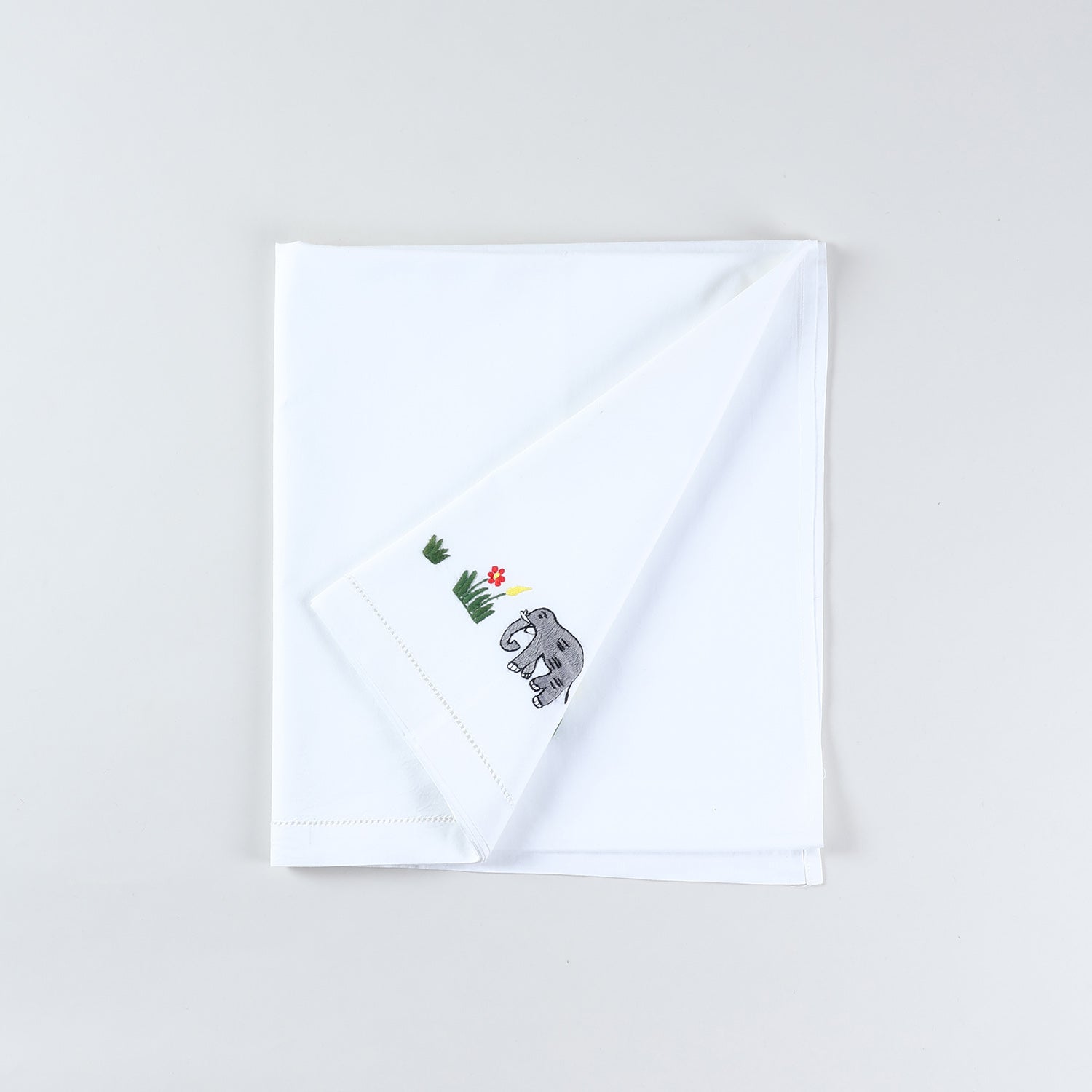 White cotton kids bedsheet folded back diagonally to showcase colourful elephant embroidery motifs handcrafted on a soft cotton base