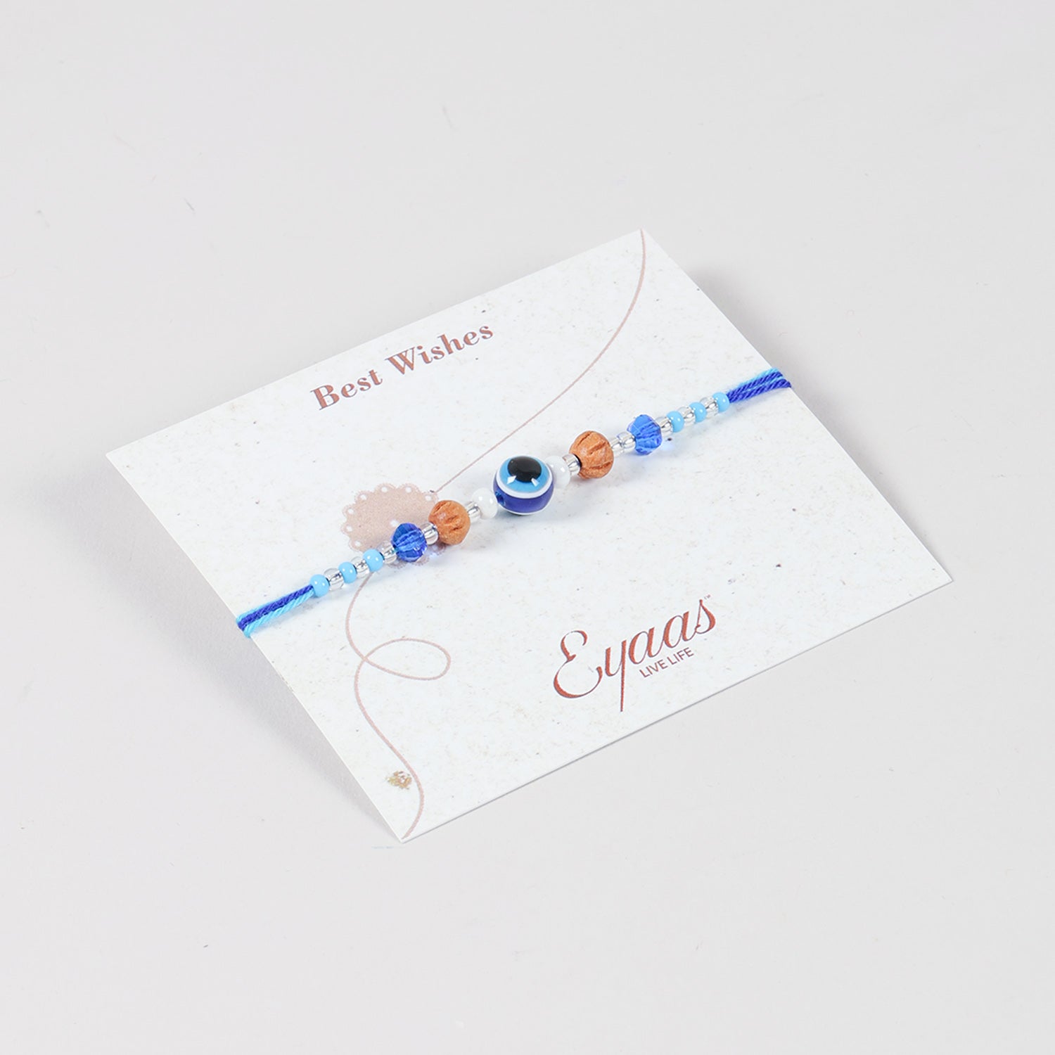 Angled view of the Handmade Evil Eye Rakhi with Beads attached to a Best Wishes greeting card for Raksha Bandhan gifting.