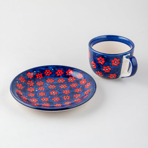 Angled view of a handpainted ceramic mug with matching saucer, showcasing floral artwork and glossy ceramic finish