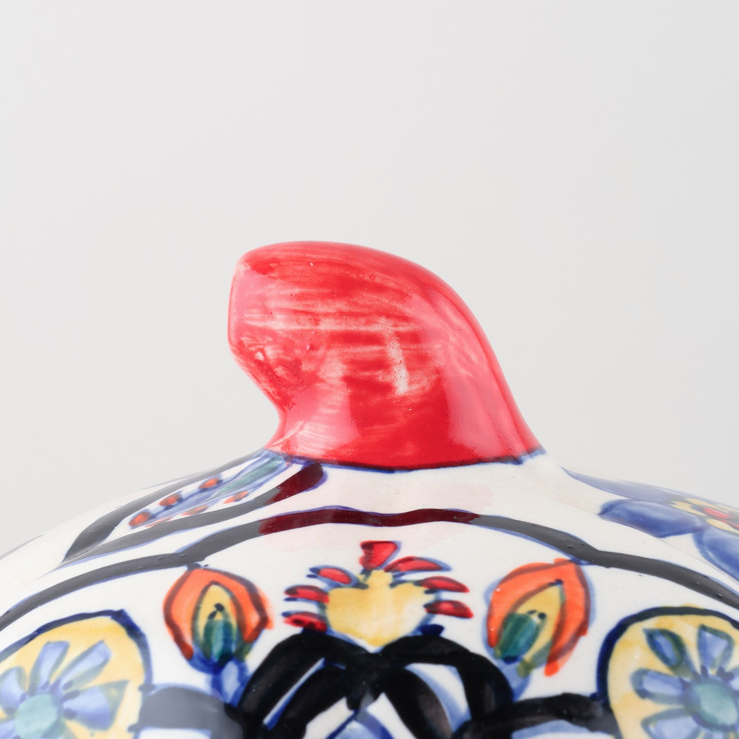 A close-up shot of the top of a white ceramic pumpkin candle holder crafted by Khurja artisans, focusing on its curved, colourful stem 