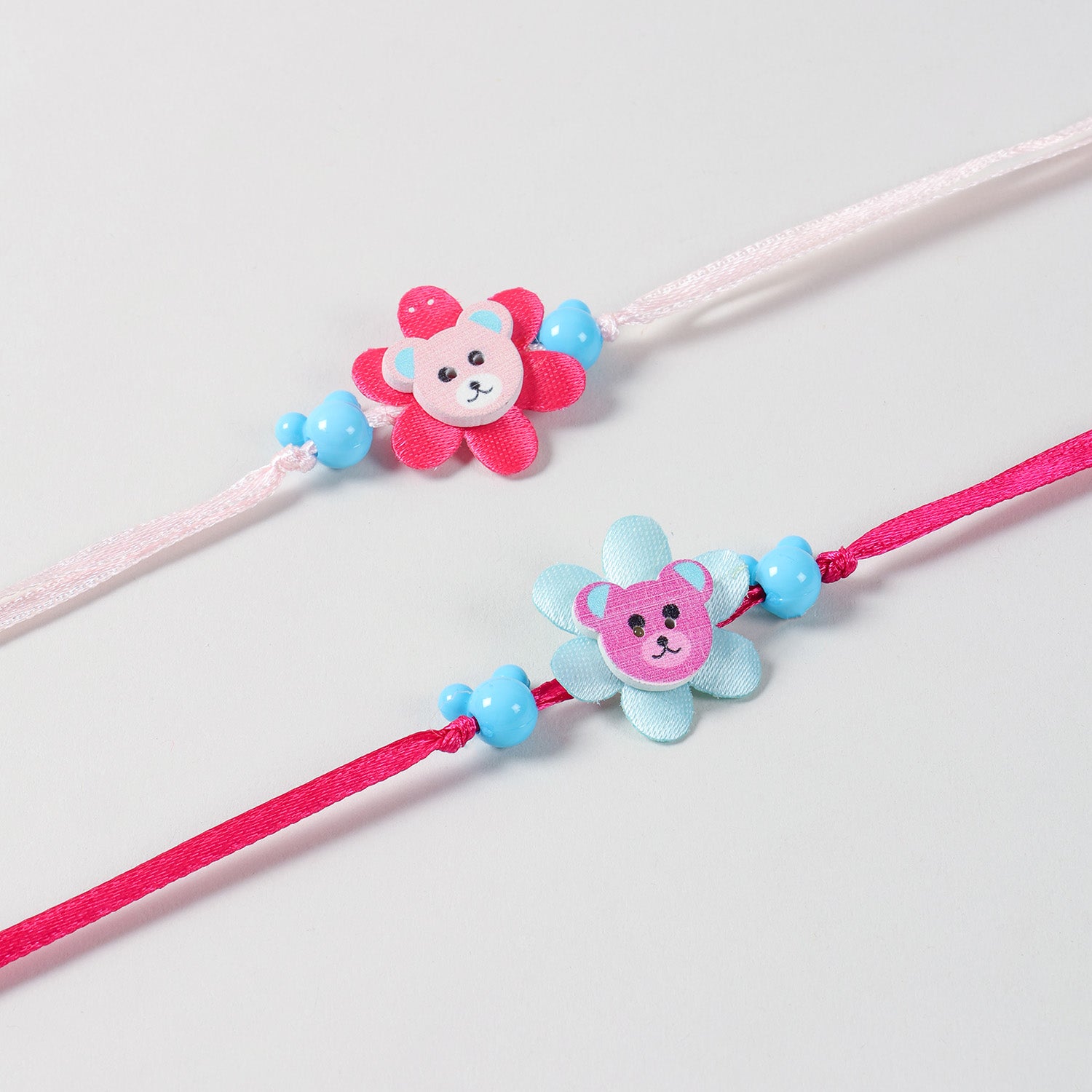Close-up of the Floral Ribbon Wooden Teddy Bear Kids Rakhi  Set of 2 featuring colourful blue and pink teddy designs with soft ribbon details