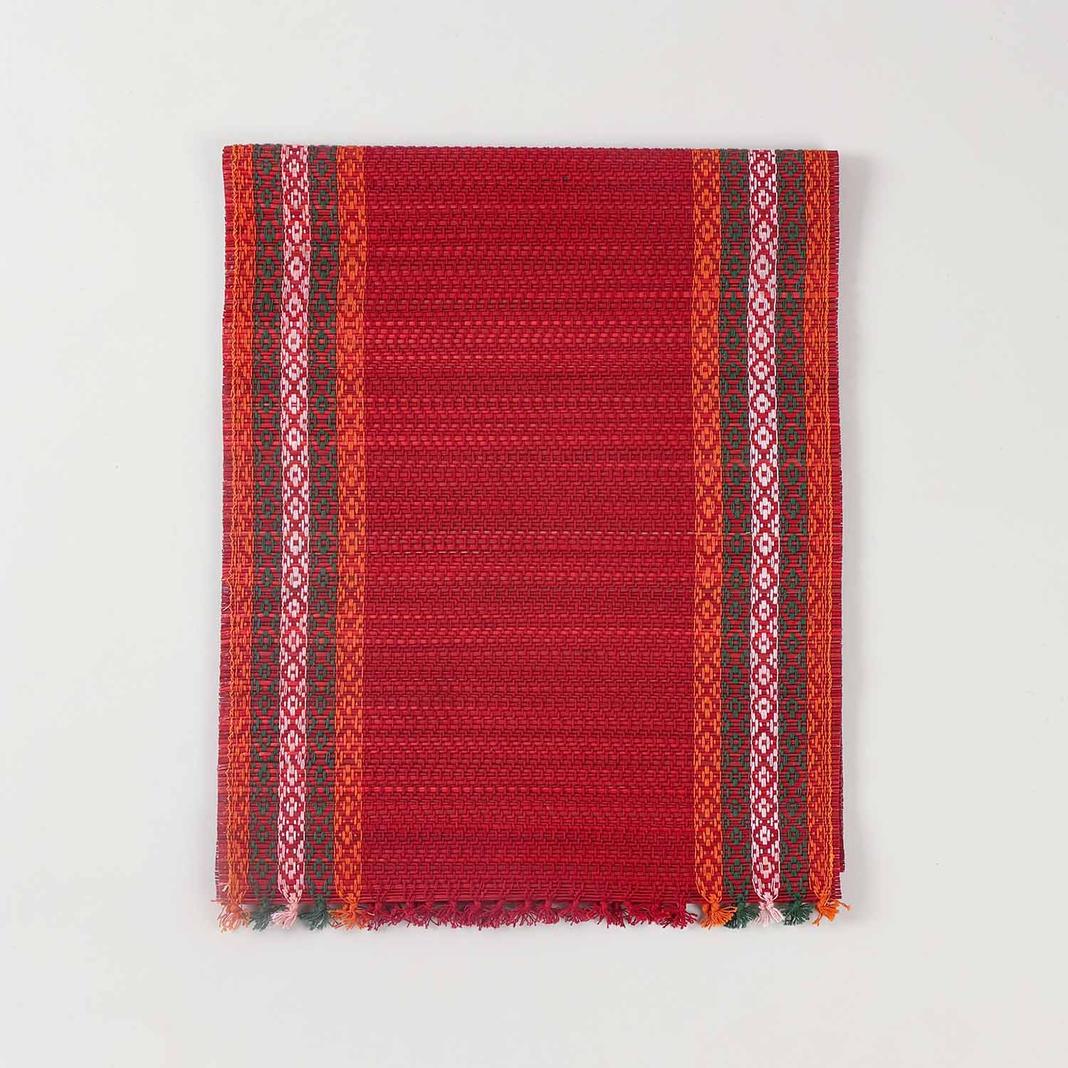 Folded red Madurkathi table runner crafted from natural river grass with handwoven texture and contrasting border details