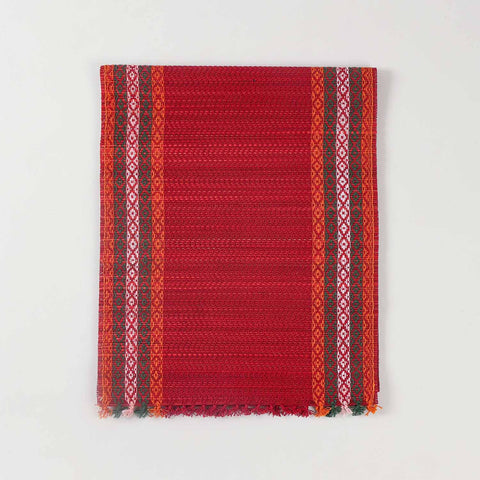 Folded red Madurkathi table runner crafted from natural river grass with handwoven texture and contrasting border details