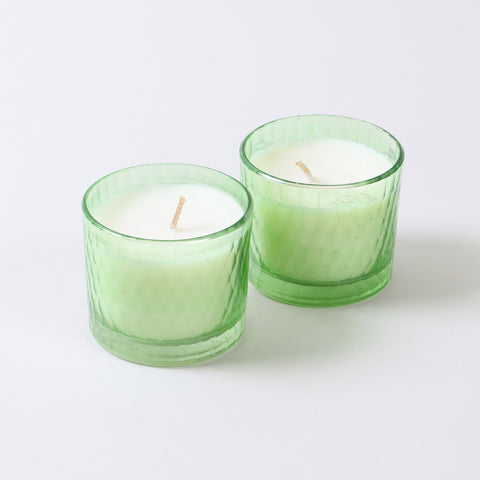 Two small green apple scented soy wax candles in green glasses on a clean background