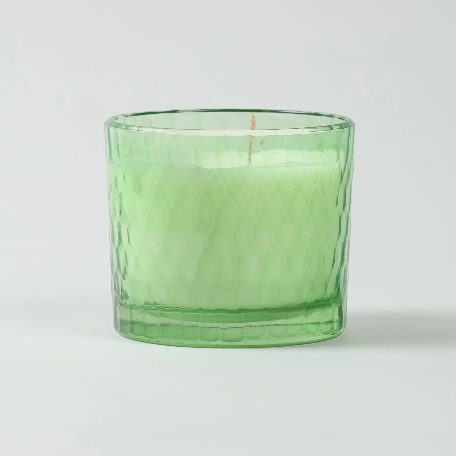 Eye-level view of a green apple scented soy wax candle showcasing the decorative chiseled glass design