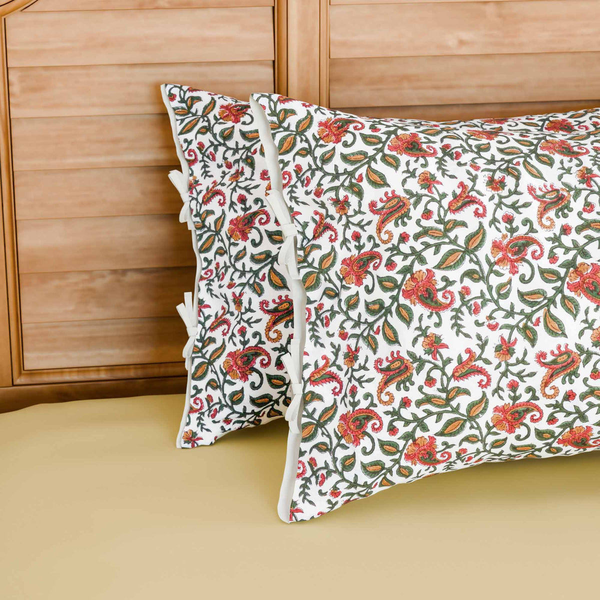Hand block printed cotton pillow cover set featuring green and pink paisley jaal motifs on a white base, styled on a bed with coordinated cotton bed linen