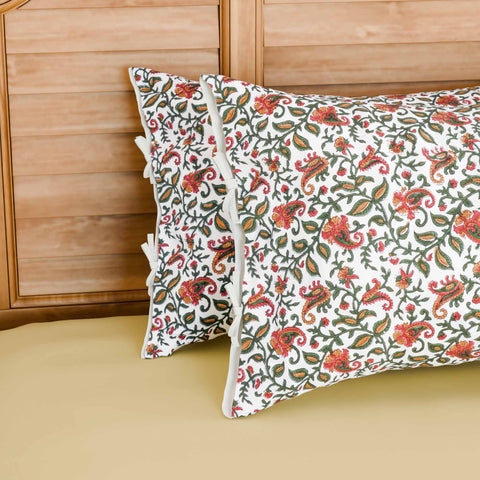 Hand block printed cotton pillow cover set featuring green and pink paisley jaal motifs on a white base, styled on a bed with coordinated cotton bed linen