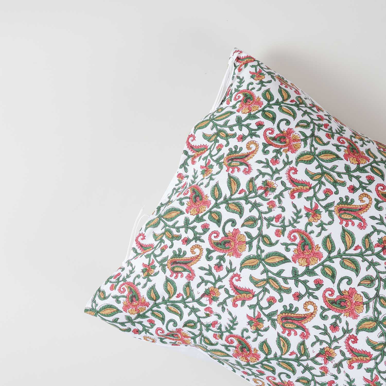 Angled close-up of cotton pillow cover fabric featuring traditional hand block printed paisley jaal motifs in green, pink, and mustard colours