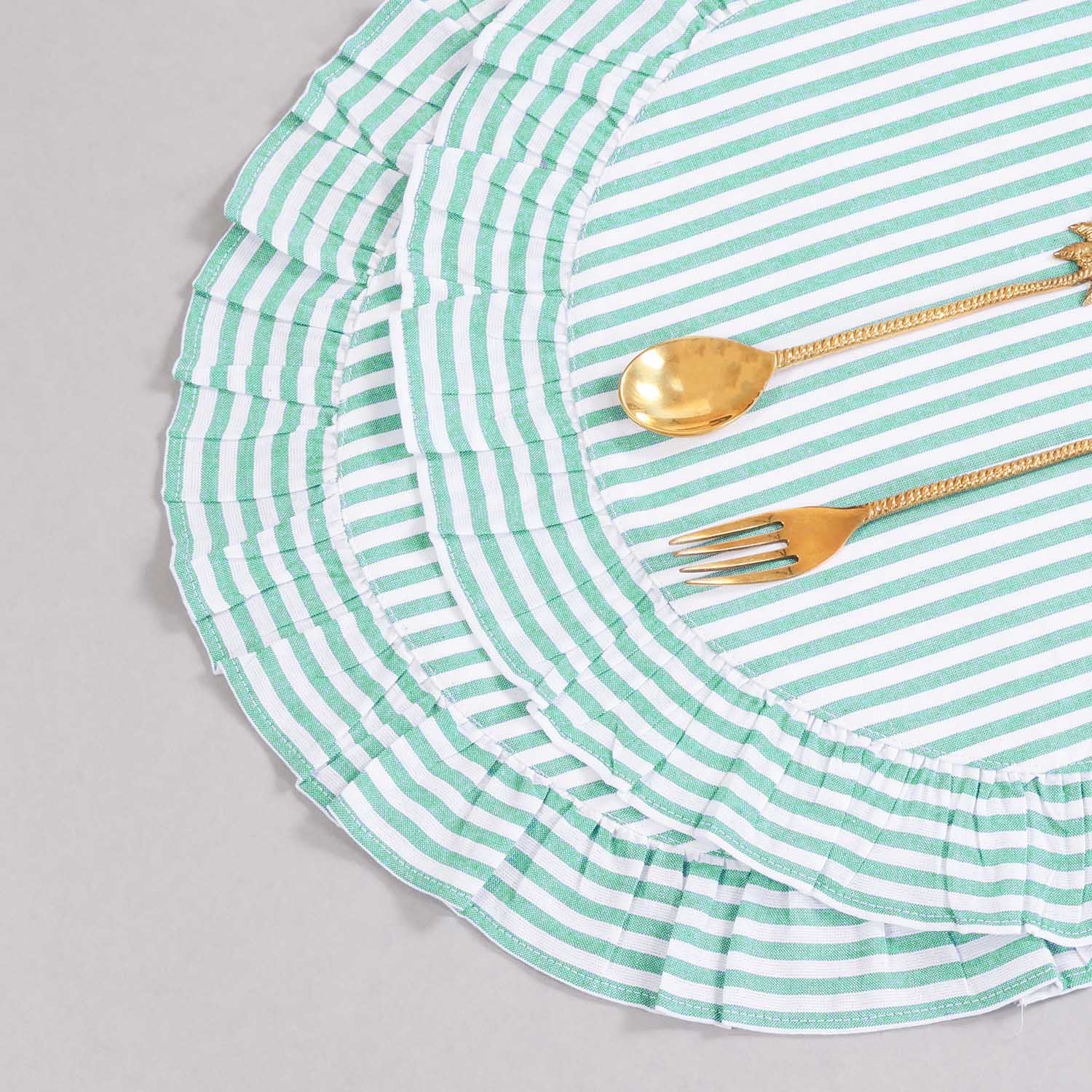 Angled top view of two round cotton placemats styled with flatware, showcasing green stripes, frilled edging, and handcrafted detailing