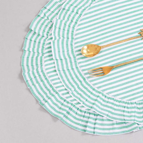 Angled top view of two round cotton placemats styled with flatware, showcasing green stripes, frilled edging, and handcrafted detailing