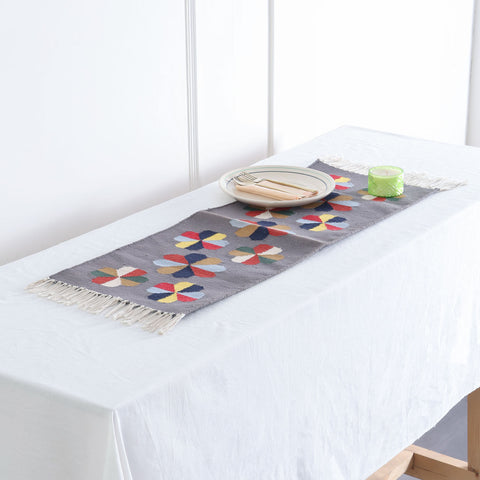 Grey handwoven cotton floor runner with colourful geometric floral motifs styled in a table  as a decorative home accent