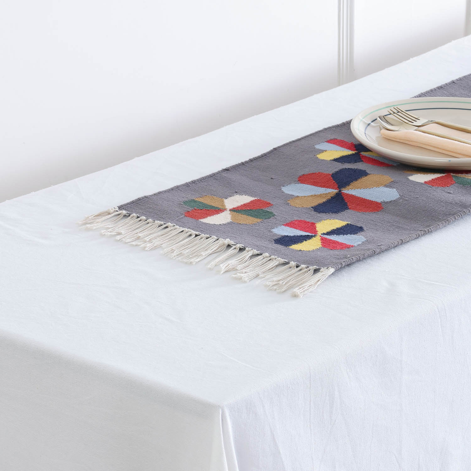 Detailed view of tasseled fringe a handwoven cotton floor runner featuring colourful geometric flower designs on a grey background