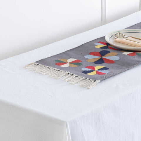 Detailed view of tasseled fringe a handwoven cotton floor runner featuring colourful geometric flower designs on a grey background