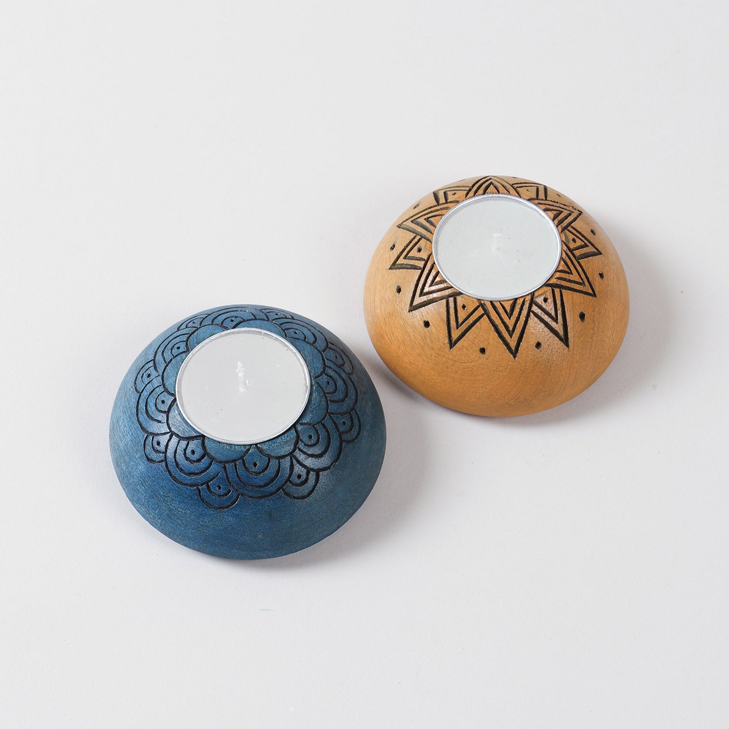 Angled view of a handcrafted wooden T-light holder set showcasing blue scalloped carving and yellow sun design details