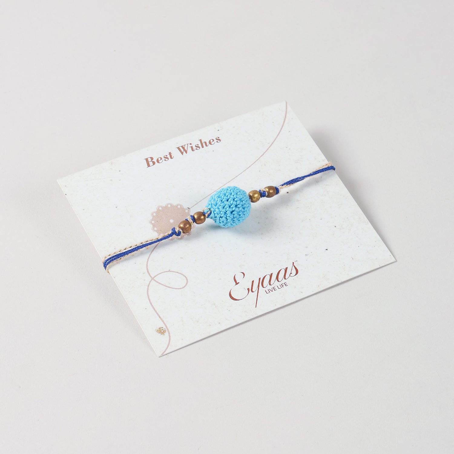 Angled view of the Handmade Crochet Bead Rakhi attached to a festive Best Wishes card for Raksha Bandhan gifting.