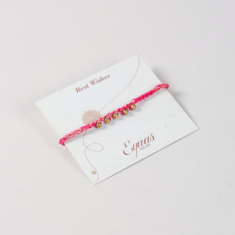 Angled view of the Handmade Crochet Brass Bead Rakhi with pink and golden threads attached to a festive Best Wishes card for Raksha Bandhan gifting.