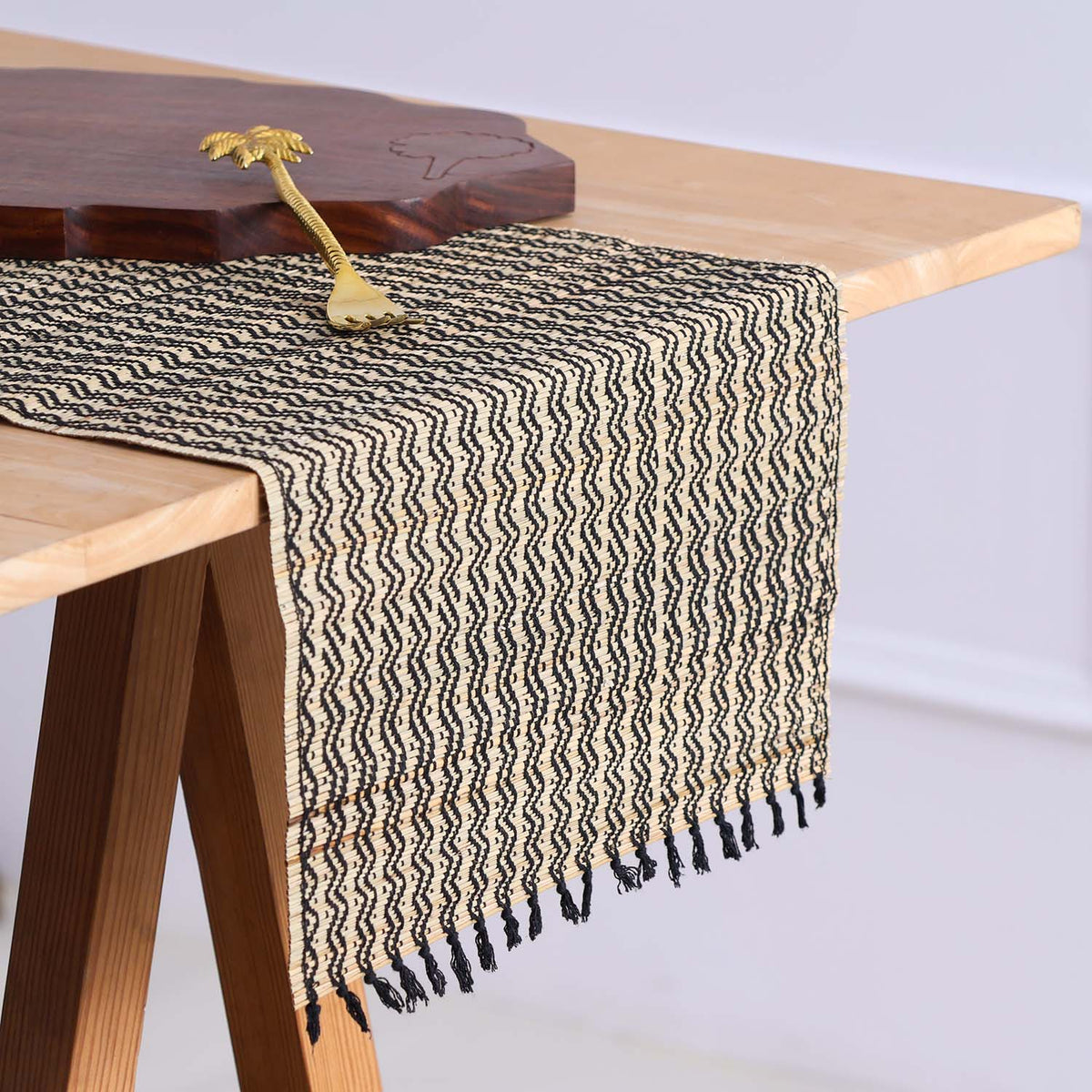 Handmade Madhurkathi table runner styled on a dining table, highlighting the natural river grass weave, black tassels, and earthy table setting