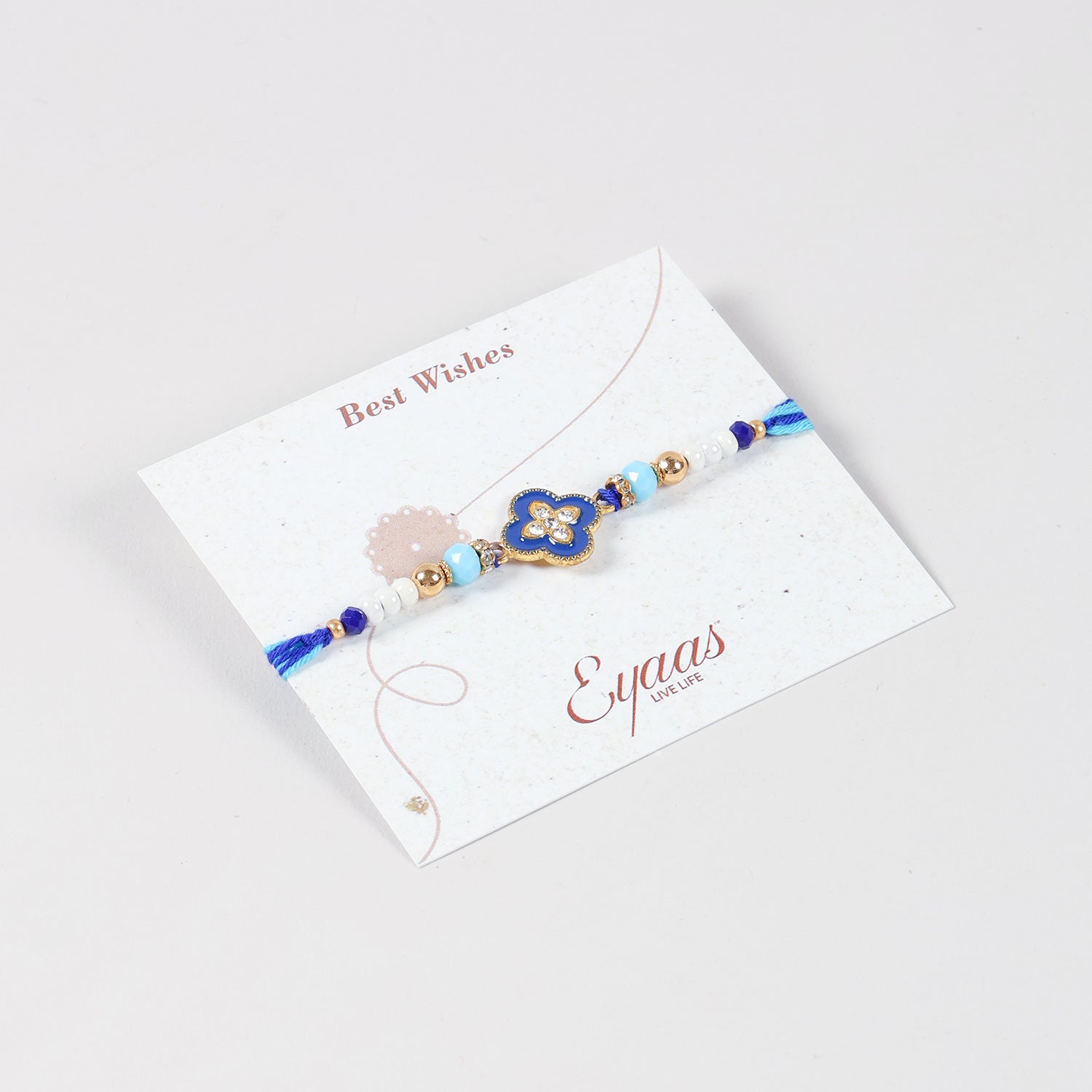 Angled view of the Handmade Metal Floral Rakhi attached to a Best Wishes greeting card for Raksha Bandhan gifting.