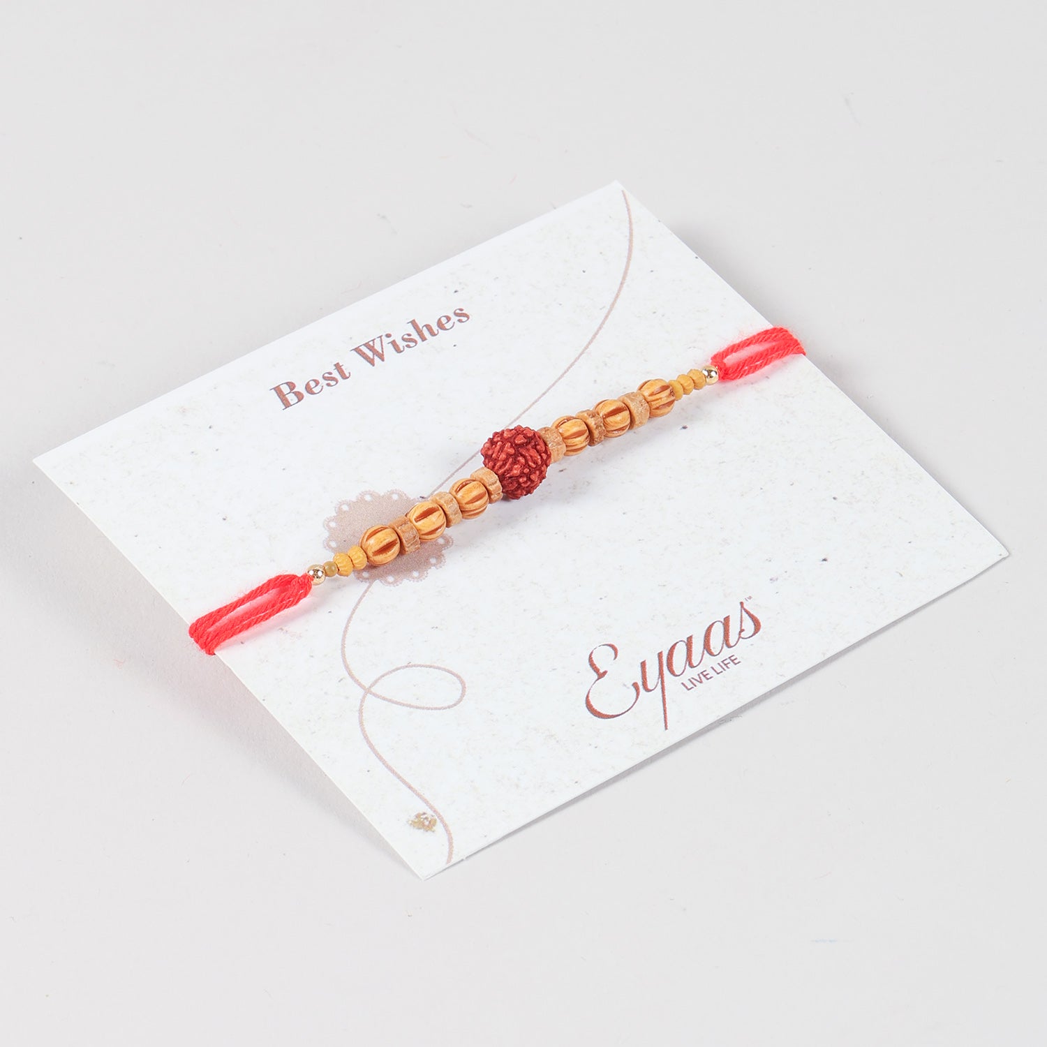 Angled view of the Handmade Rudraksha & Wooden Bead Rakhi attached to a Best Wishes greeting card.