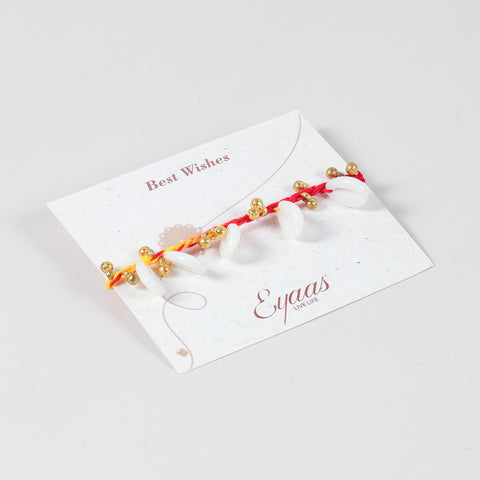 Angled view of the handmade sea shell & Ghungroo Rakhi attached to a Best Wishes greeting card for Raksha Bandhan gifting.
