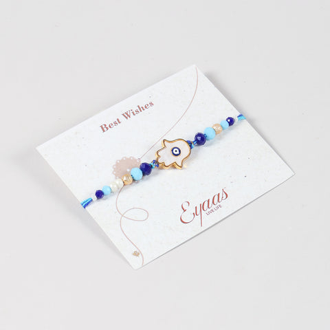 Angled view of the Handmade White Hamsa Evil Eye Rakhi attached to a Best Wishes greeting card for Raksha Bandhan gifting.