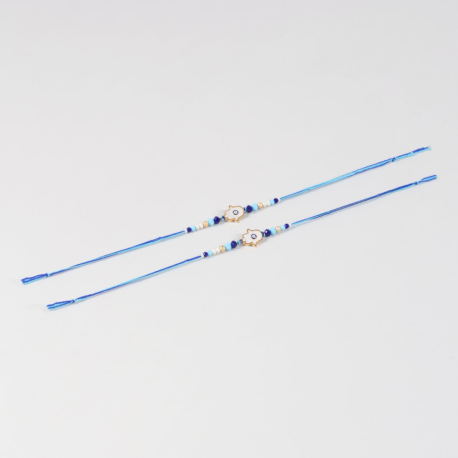 Full-length view of the Handmade White Hamsa Evil Eye Rakhi Set of 2 showing the complete handcrafted design and blue cotton thread.