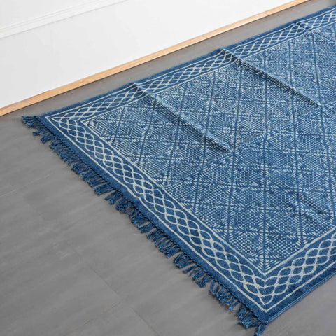 Oblique high-angle view of an indigo handloom dhurrie rug displaying geometric block-printed patterns and overall layout