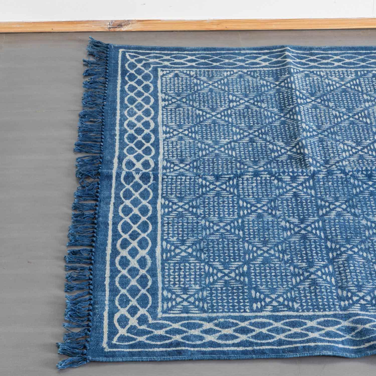 Top view of an indigo cotton dhurrie rug highlighting geometric hand block printed motifs and woven fringe detailing