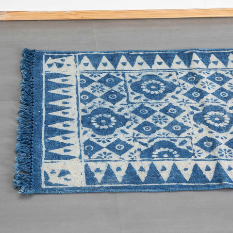 Angled view of a part of a handmade indigo dhurrie rug with geometric floral design styled in an entryway