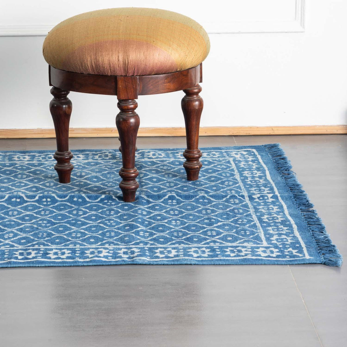 Handmade indigo diamond floral dhurrie rug styled in a reading corner, showcasing traditional weaving and block printing