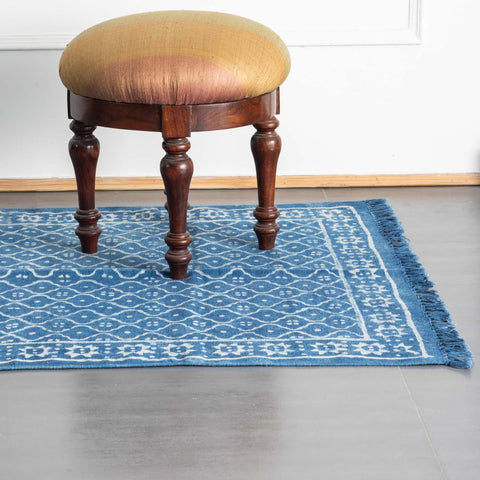 Handmade indigo diamond floral dhurrie rug styled in a reading corner, showcasing traditional weaving and block printing