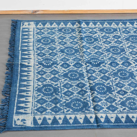 Top view of an indigo cotton dhurrie rug, highlighting geometric floral block prints and woven fringe detailing