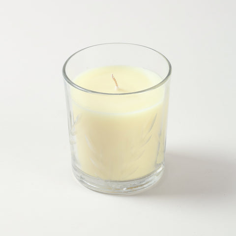 Close-up of white glass candle featuring embossed leaf design and natural soy wax filling