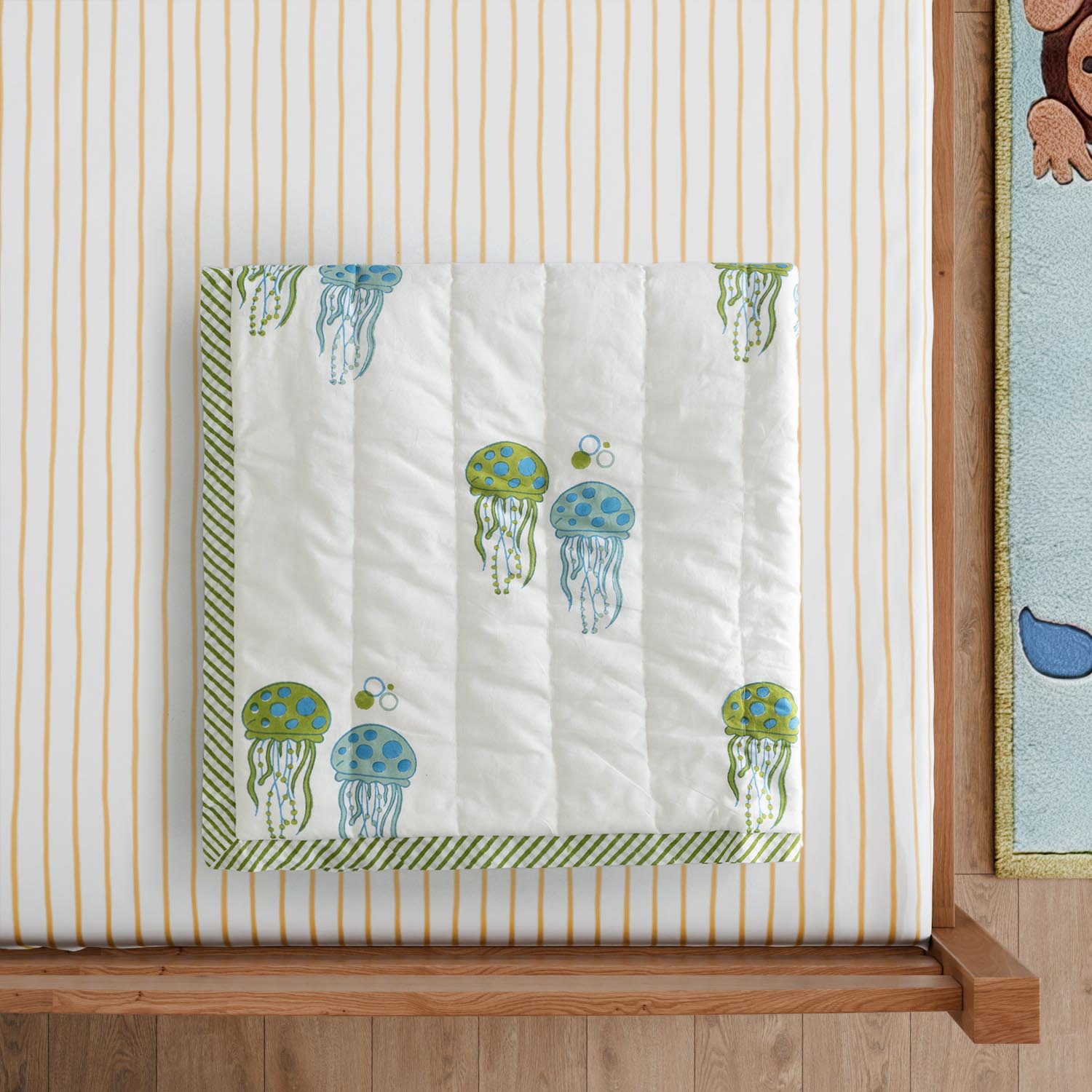 Styled close-up of a reversible cotton quilt featuring hand block printed jellyfish motifs in blue and green, showcasing soft breathable cotton fabric and detailed artisan craftsmanship