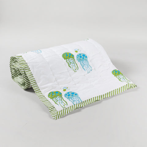 Angled view of a rolled reversible cotton quilt with blue and green jellyfish prints, perfect as a lightweight quilt for travel and daily use