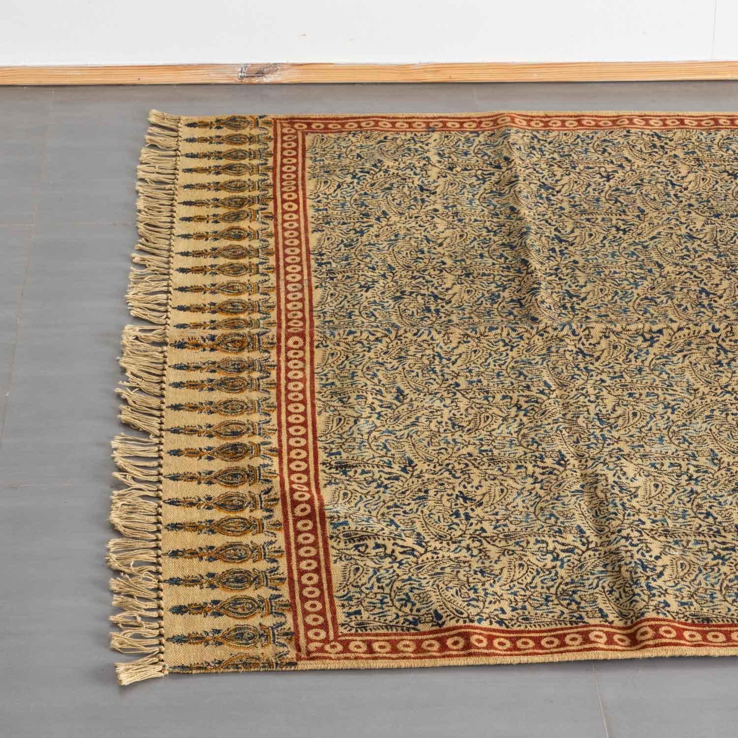 Top view of a mustard cotton dhurrie rug highlighting Kalamkari block prints and woven fringe detailing