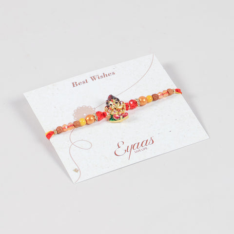 Angled view of the Handmade Kids Metal Ganesh Rakhi attached to a Best Wishes greeting card for Raksha Bandhan gifting.