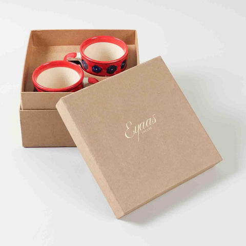 Open gift box displaying two large floral red ceramic coffee mugs ready for gifting