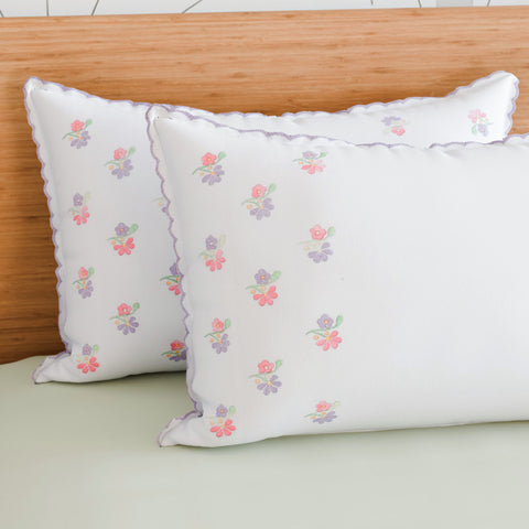 Lavender chikankari embroidered pillow cases styled on a bed with soft cotton bedding and wooden headboard