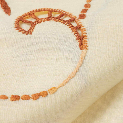 Close-up of embroidery on a light brown bedcover, highlighting intricate handcrafted threadwork and fabric texture