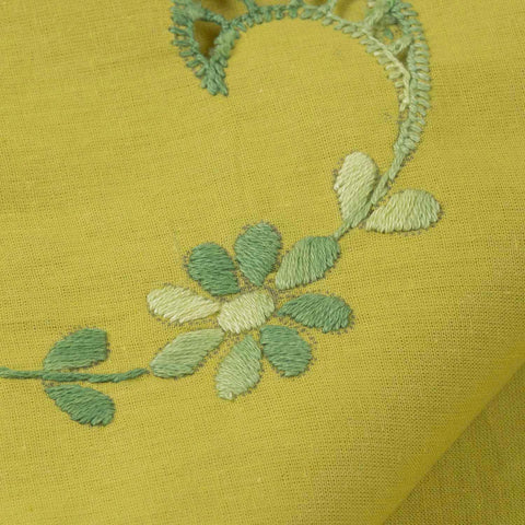 Close-up of floral chikankari embroidery in green thread on a light green cotton bedcover, highlighting artisan craftsmanship