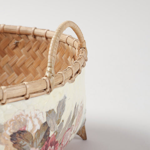 Close-up of a handmade Naga basket showing woven bamboo craftsmanship, curved handle, stitched rim, and pink floral decoupage artwork