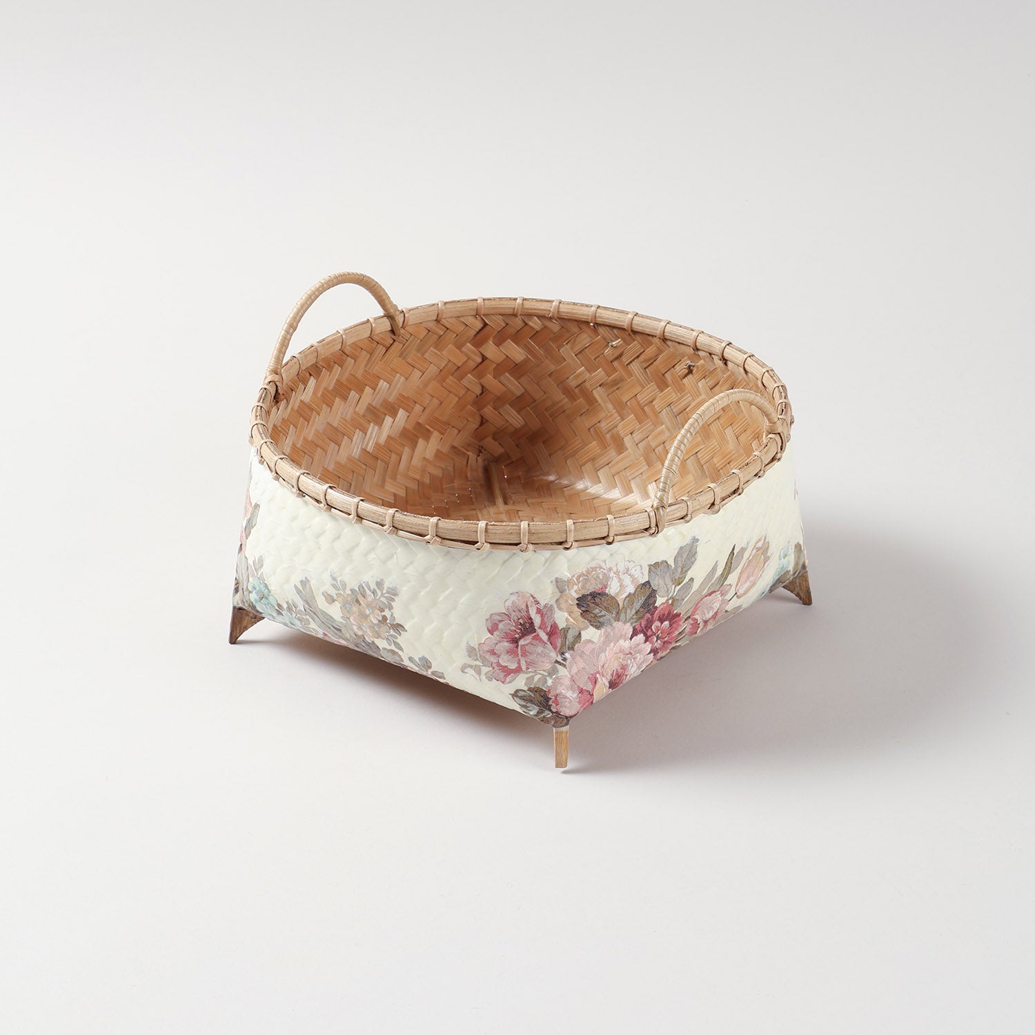 Square wicker storage basket with pink floral decoupage design, double handles, and raised wooden feet for stylish home organisation