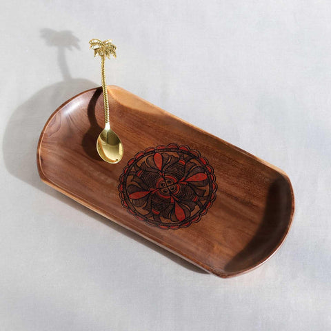 Wooden tray cum platter with fish motif and gold spoon on a light gray background