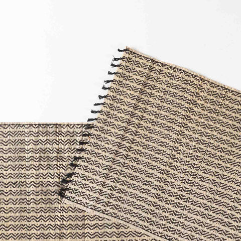 Close-up of a Madhurkathi table runner featuring intricate zigzag weave patterns, natural fibre texture, and dark fringe tassels